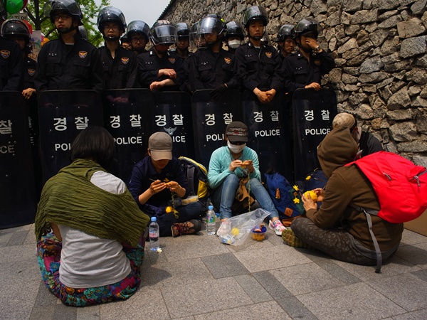 경찰들 앞에서 뜨개질을 하고 있는 사람들