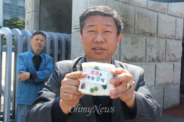  홍준표 경남지사가 8일 오전 성완종 리스트와 관련해 검찰에 출석한 가운데, '경남도청과 공공기관 이전반대 창원시민대책위' 변상기 공동집행위원장이 '준표표 무상콩떡'이라 적힌 떡을 만들어 와 창원지방검찰청 앞에서 들어 보이고 있다.