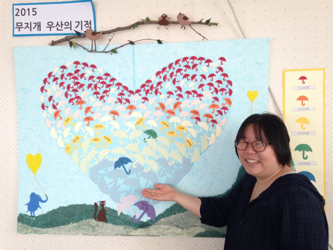 후원회원들의 이름이 적힌 '무지개 우산의 기적' 앞에 선 윤다림 간사