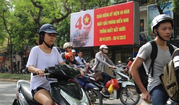 오토바이를 탄 하노이 시민들이 40년 전 독립궁에 진입한 탱크를 그려 넣은 베트남전 40주년 알림판 앞을 지나고 있다.