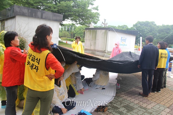  20일 친환경무상급식지키기 경남운동본부 진헌극, 전진숙 공동대표가 '무상급식 원상회복' 등을 요구하며 경남도청 정문 옆에서 나흘째 단식농성하고 있는 가운데, 빗방울이 떨어지자 차양막을 설치하고 있다.