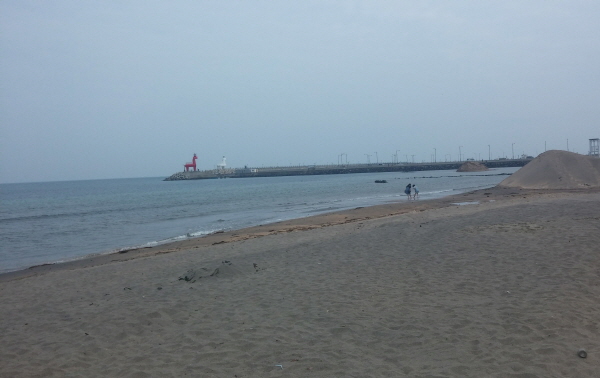 저 멀리 빨간 등대, 하얀 등대가 보이고 해변가엔 친구 두 명이 바다에 발을 담그고 놀고 있다.