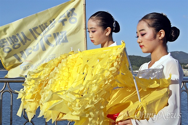 공연에 앞서 팽목항 방파제에서 진행된 침묵 순례 도중 어린 학생들이 노란 모형 배를 들고 '정부 쓰레기 시행령 폐기'라고 적힌 깃발 앞을 지나고 있다.