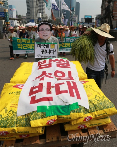 지난 7월 31일 오후 서울 용산구 서울역광장에서 열린 전국농민대회에 참석한 한 농민이 박근혜 정부와 새누리당의 밥쌀용 쌀 수입 정책을 규탄하며 이동필 농식품부 장관의 가면을 쓴 채 수입쌀을 손수레에 싣고 거리행진을 벌이고 있다.