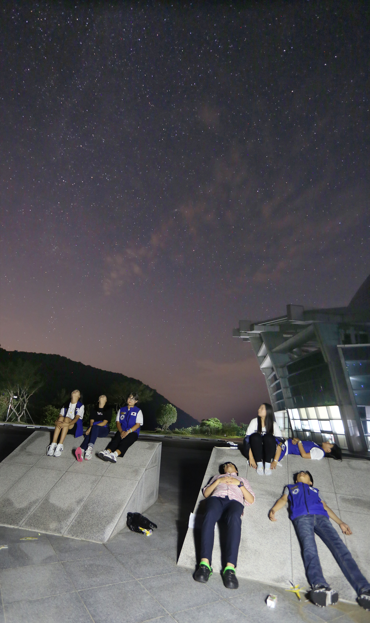 페르세우스 유성우를 마음에 담기 위해 광장에 모인 청소년이 은하수 아래에 누워 하늘을 바라보고 있다.