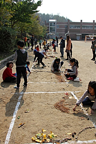 학교 운동장 도화지에 가을 풍경을 그리고 있는 학생들 