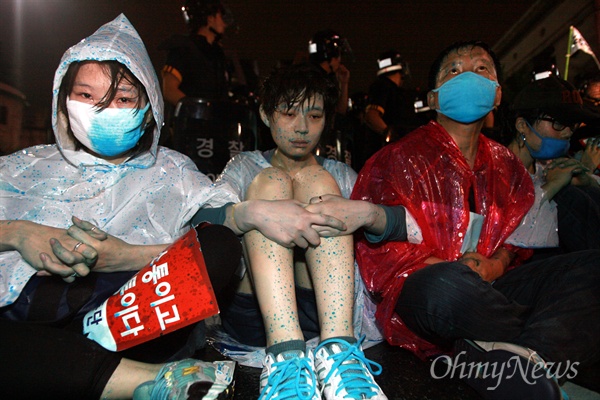  15일 저녁 서울 한국은행앞에서 제100차 촛불집회에 참석하는 시민들을 경찰이 강제해산시키는 가운데, 파란 색소를 섞은 물대포를 뒤집어 쓴 '815평화행동단' 회원들이 연좌 시위를 벌이고 있다.