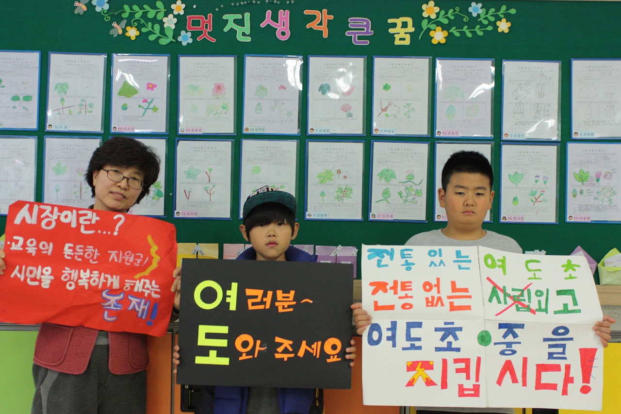 여도초 5학년 2반 박미경 선생님과 이정호(가운데), 김경민 학생이 학교를 지키기 위해 한달간 피켓시위를 했다. 당시 사용한 피켓을 들어보이고 있다.