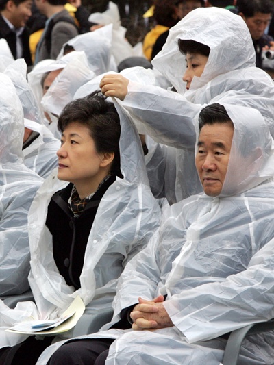 지난 2005년 2월 18일 가랑비가 내리는 가운데 진행된 대구지하철 참사 희생자 추모식에서 당시 한나라당 전여옥 대변인이 박근혜 대표의 비옷에 달린 모자를 씌워주고 있다.