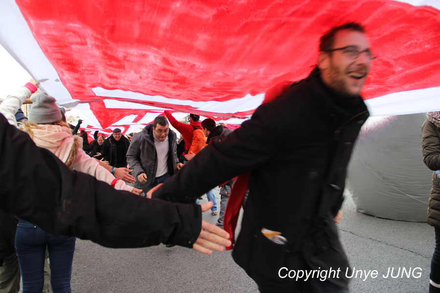 파리회의 190개국 대표들이 이번 회의에서 넘지 말아야 할 선을 상징하는 붉은 띠를 높이 들어 터널을 만들었다. 가두시위에 참여하는 시민들이 환호를 하며 달려가고, 이들을 환영하는 의미로 하이파이브를 해주고 있다. 