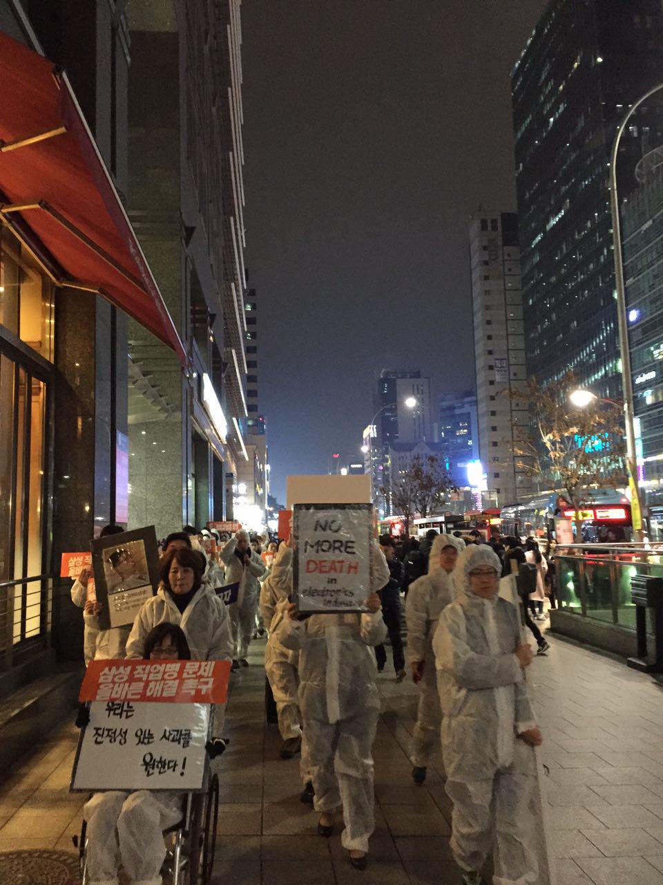 방진복을 입은 시민과 삼성직업병 피해자들이 행진하고 있다. 