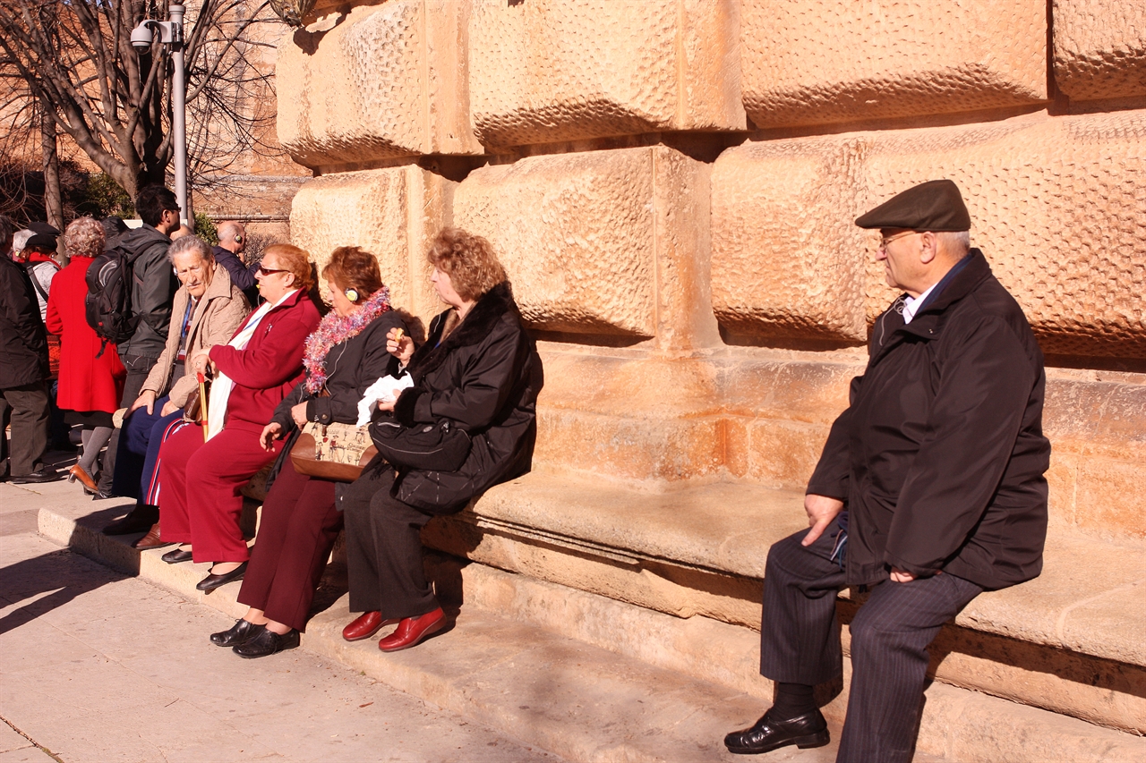 스페인 관광객들이 카를로스 5세 궁전 벽에 등을 기대고 볕을 쬐며 쉬고 있다.