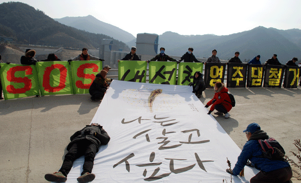 시민환경단체들이 영주댐이 바라다보이는 진입로에서 'SOS 내성천 영주댐 철거' 문구와 대형 흰수마자가 그려진 현수막을 들고 담수 중단을 요구하고 있다. 