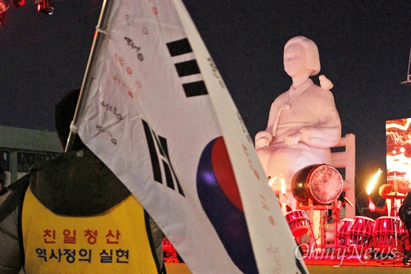 '친일 청산, 역사 정의 실현'이라고 적힌 조끼를 입은 한 시민이 태극기를 든 채 이날 무대 위에 설치된 높이 6m의 소녀상을 바라보고 있다.