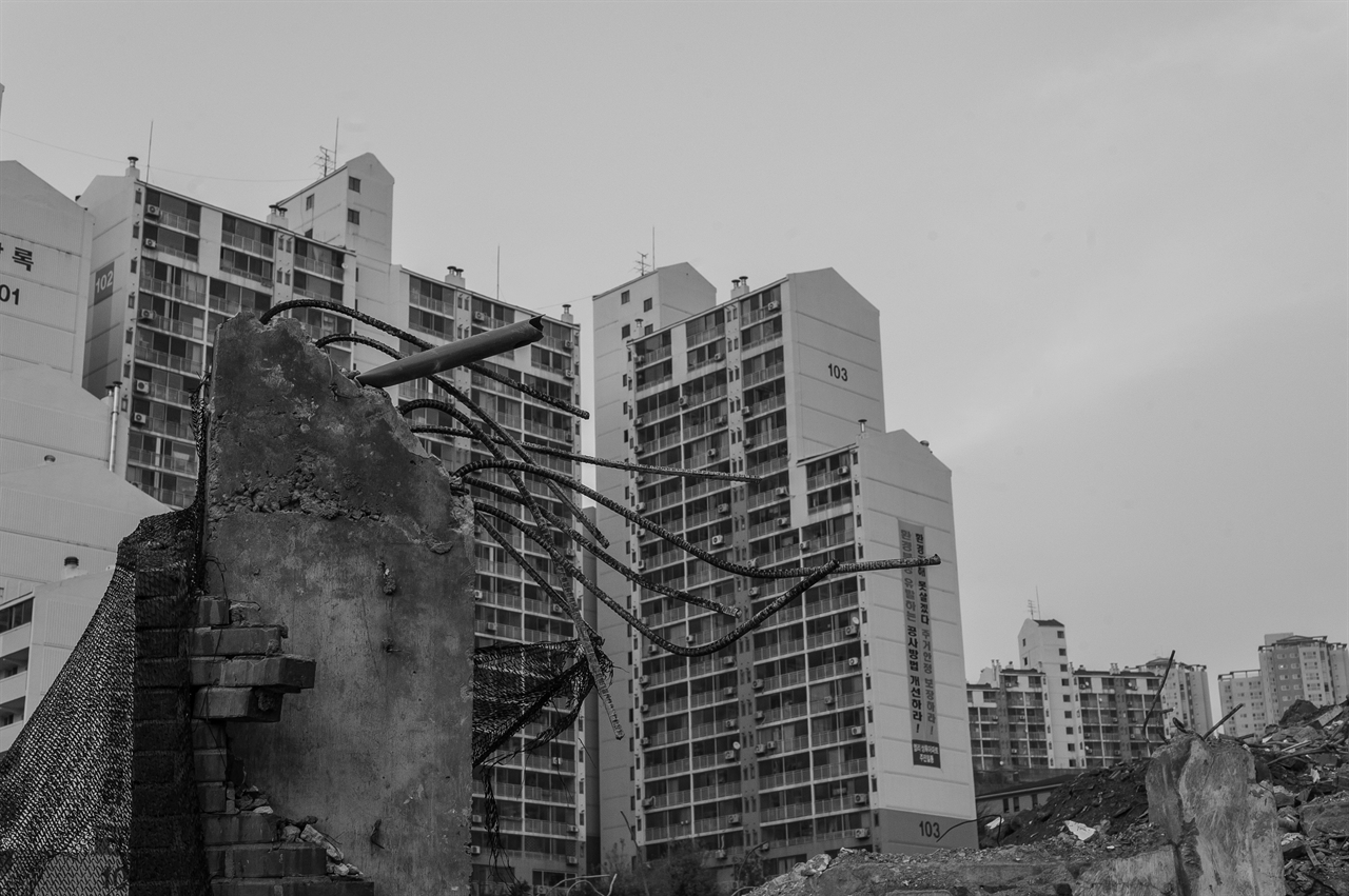 2015년 11월 20일, 염리동 철거된 집의 잔해 넘어로 고층 아파트가 보인다. 가까워 보이지만 아파트와 철거가 진행중인 지역은 사실상 완전히 분리되어 있다.