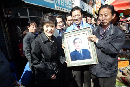 지난 2004년 3월 청량리 시장에서 초상화를 팔던 한 할아버지가 진열 중이던 박정희 전 대통령의 초상화를 들고와 박근혜 대표와 인사하고 있다.
