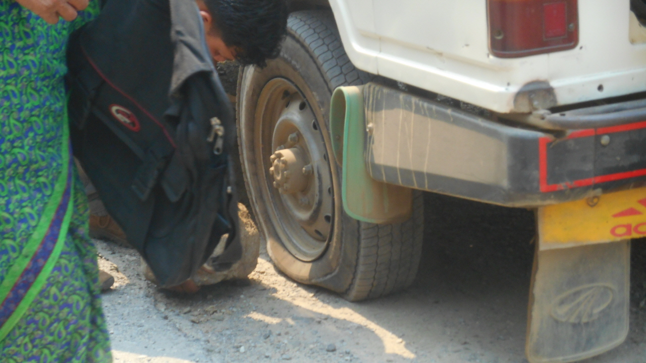 바퀴를 갈아 끼우기 위해 차제를 받쳐 놓는 자키 대신 커다란 돌멩이를 받쳐놓고 있다.