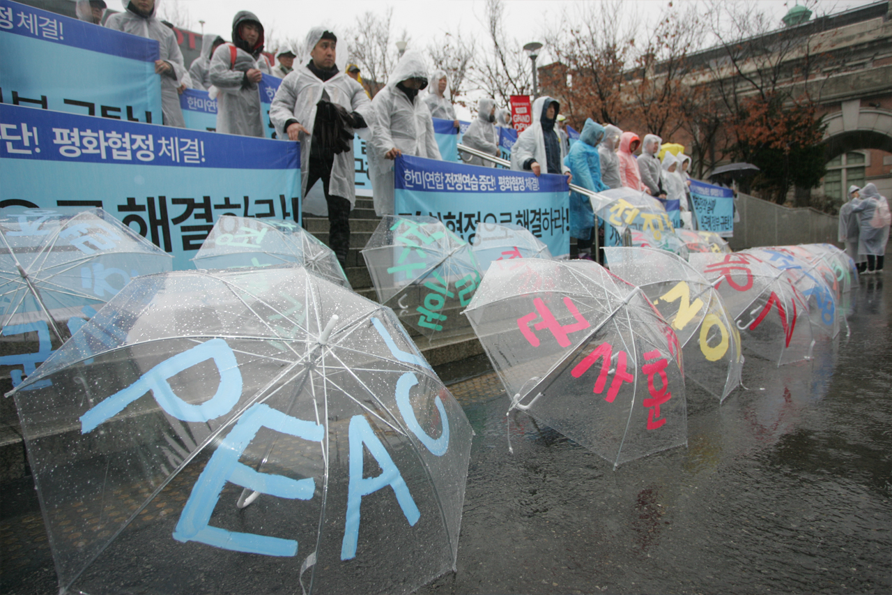 PEACE, 군사훈련 반대라고 쓰여진 우산이 비를 맞고 있다
