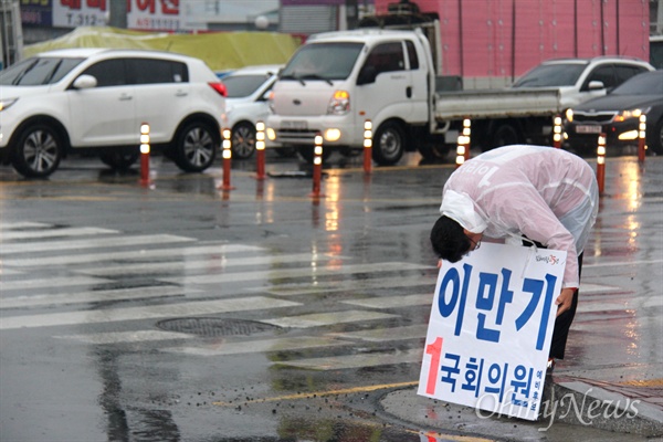 '김해을' 국회의원 선거에 나선 새누리당 이만기 후보가 18일 아침 비가 내리는 속에 김해 장유1동사무소 앞 거리에서 비옷을 입고 출근인사하고 있다.