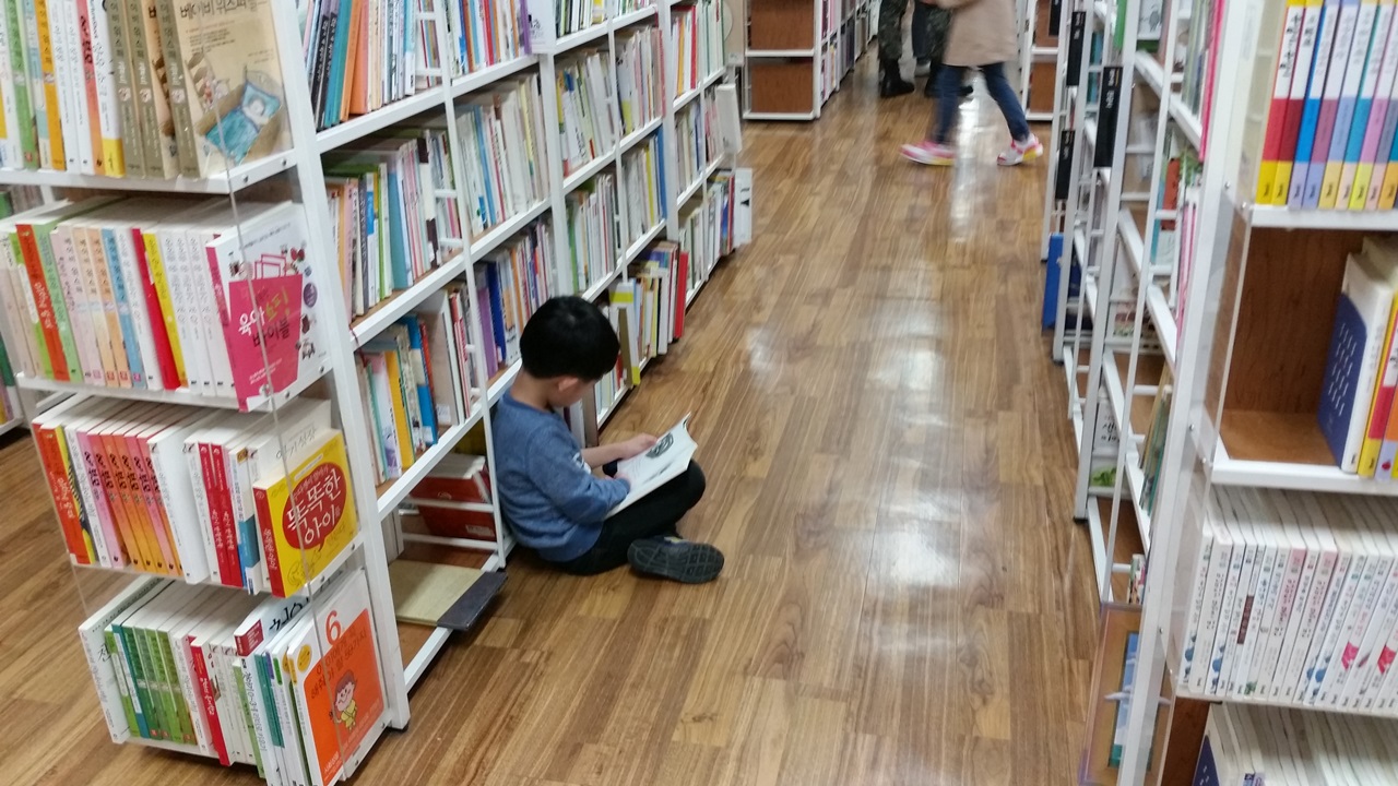 대형 중고서점 통로 바닥에 앉아 책을 읽고 있는 아이.