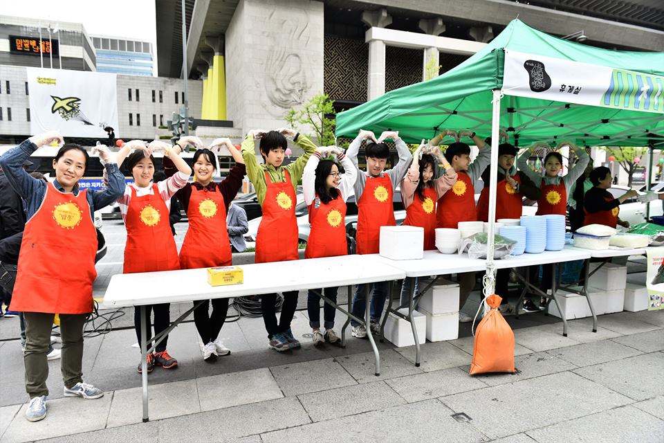 배식 봉사를 나온 학생들이  두 팔로 하트를 그려보이고 있다.