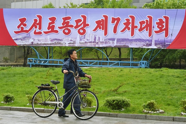 '김정은 시대'의 선포를 공식화하는 북한의 제7차 노동당 대회가 6일 열렸다. 사진은 대회가 열리는 평양 4·25 문화회관 주변에 설치된 당 대회 알림판 아래를 한 주민이 자전거를 끌고 지나가고 있다. 