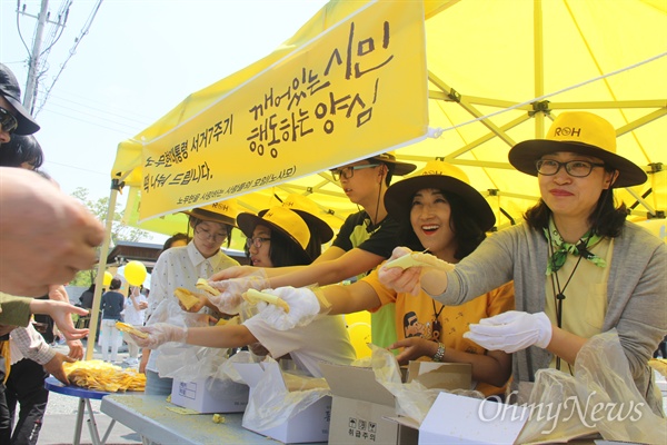  고 노무현 전 대통령 서거 7주기를 하루 앞둔 22일 경남 김해 진영읍 봉하마을에 많은 참배객들이 줄을 잇고 있는 가운데, 노사모 회원들이 사람들한테 떡을 나눠주고 있다.