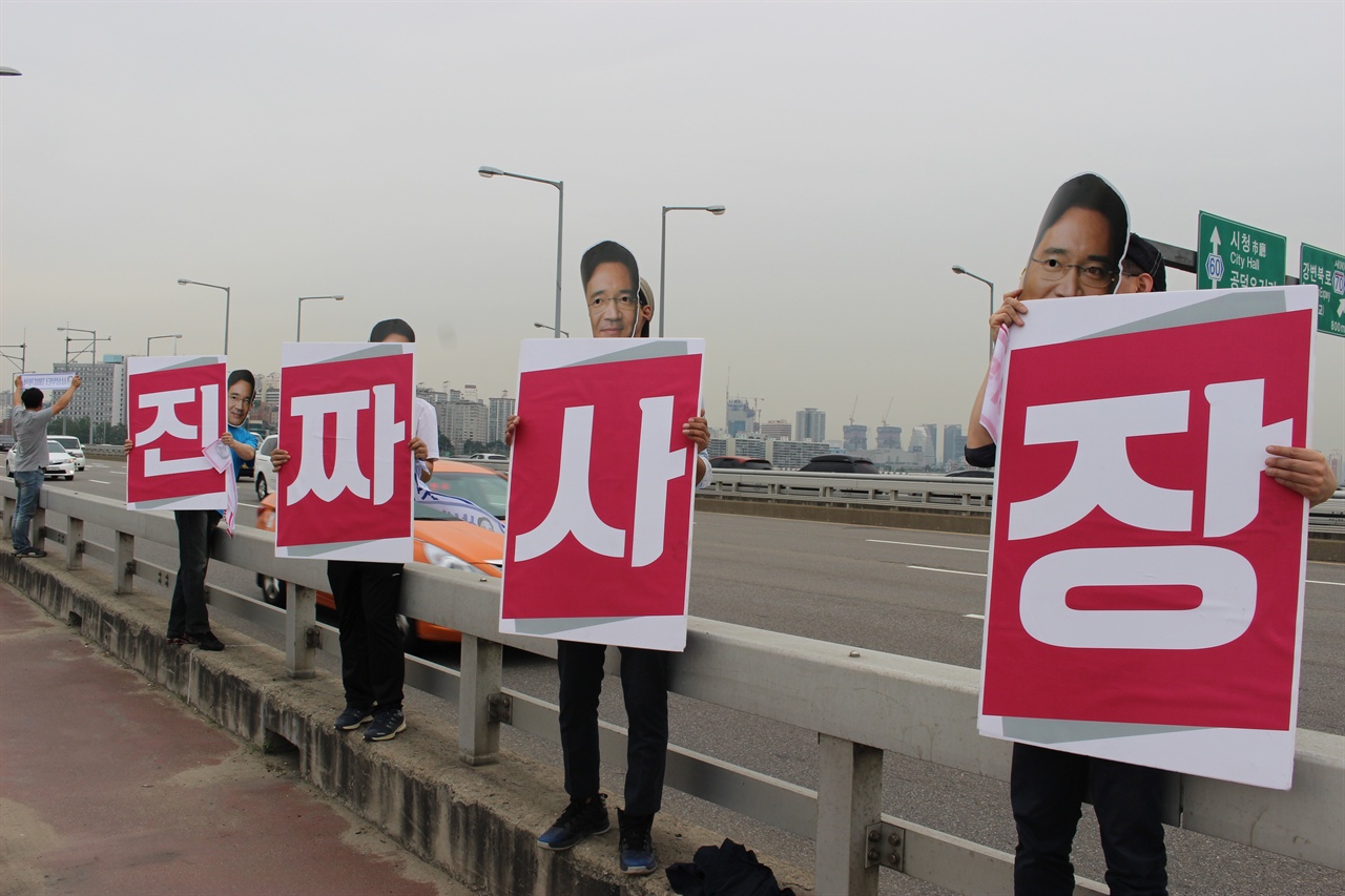6월 4일 마포대교 위에서 삼성전자서비스 AS노동자들이 삼성전자 이재용 부회장 가면을 쓴 채 '진짜사장'이라는 피켓을 들고 숨어있는 원청을 표현하고 있다.