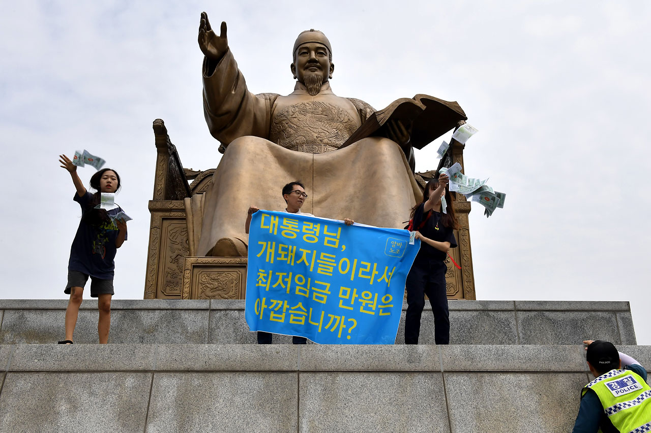  알바노조 소속 조합원들이 12일 오전 서울 세종로 광화문광장에 있는 세종대왕 동상에 올라가 최저 임금 1만원 인상을 요구하는 기습시위를 벌이고 있다.