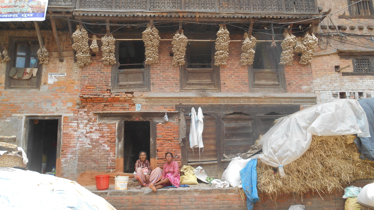 오래된 건물 앞에 앉아 있는 네팔 할머니. 처마 끝에 매달아 놓은 마늘 꾸러미들이 인상적이다.