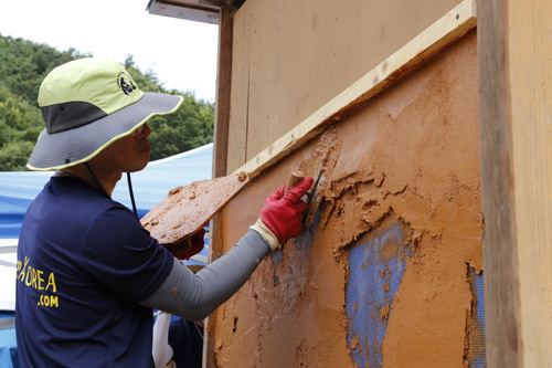 목포대학교에서 열린 흙건축 여름 캠프 참가자가 흙으로 벽체를 바르고 있다. 지난 7월 27일이다.