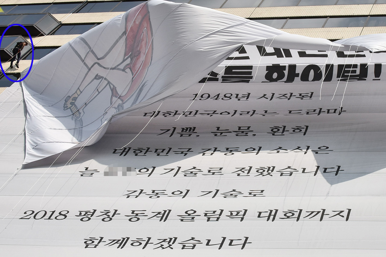 서울 종로구 세종로 인근의 한 건물외면에 '올림픽 참가 대한민국 선수단'의 선전을 기원하며 걸려있던 대형 응원현수막이 철거인력 (파란색 원안)에 의해 철거되고 있다.
