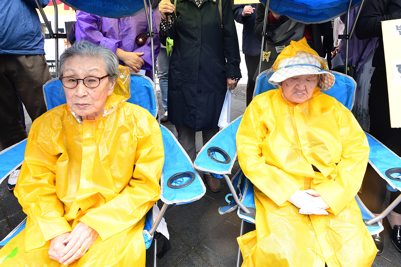  서울지역에 폭우가 쏟아지는 상황에서 김복동(왼쪽), 길원옥 할머니가 노란 우비를 입은채 31일 오전 서울 종로구 평화로 옛 일본대사관 맞은편에서 열린 '1228 한일합의 강행 규탄 및 정의로운 해결을 촉구하는 기자회견'에 참석하고 있다.