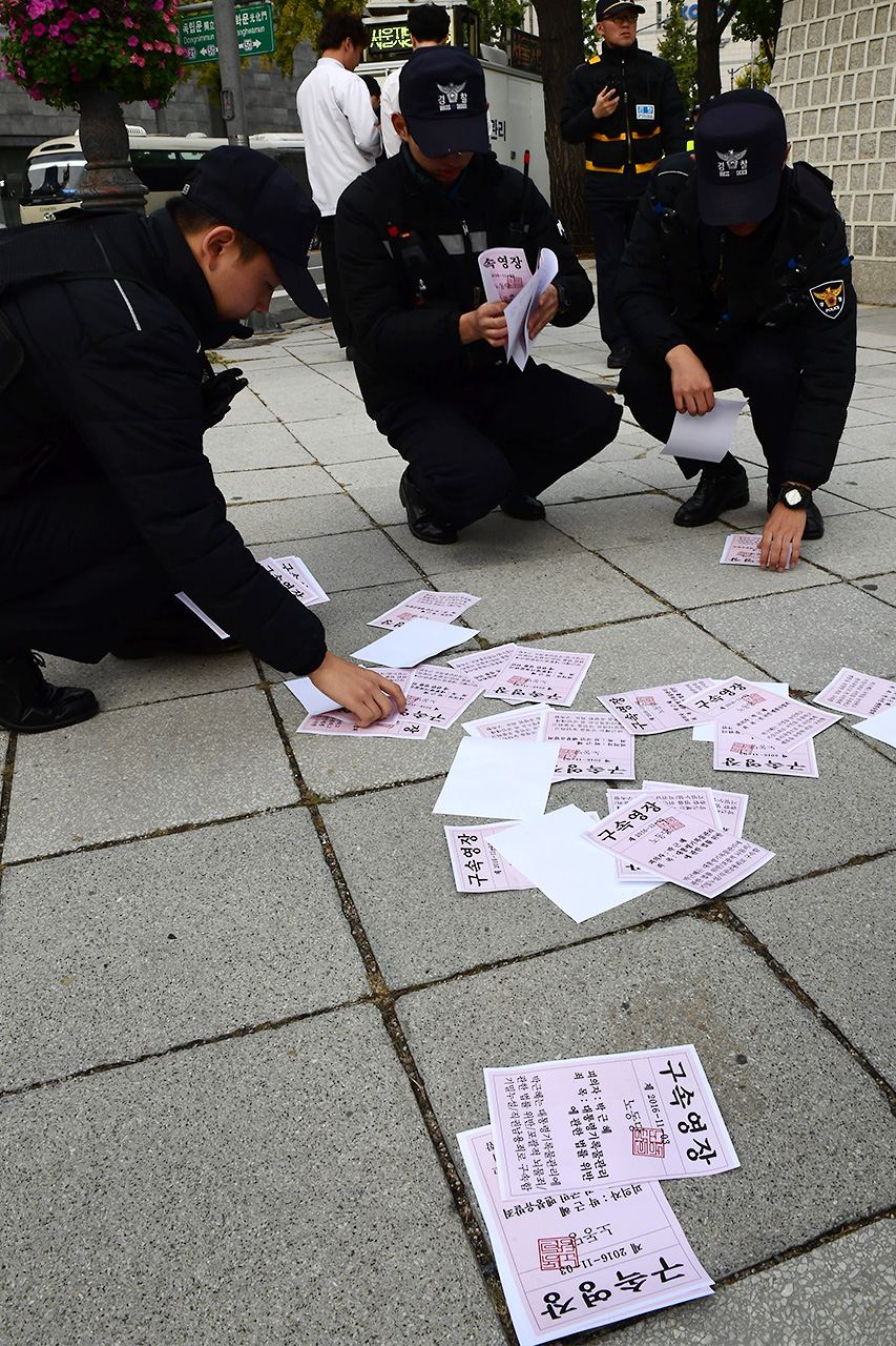 경찰들이 퍼포먼스에 사용된 '박근혜 구속영장' 유인물을 수거하고 있다. 
