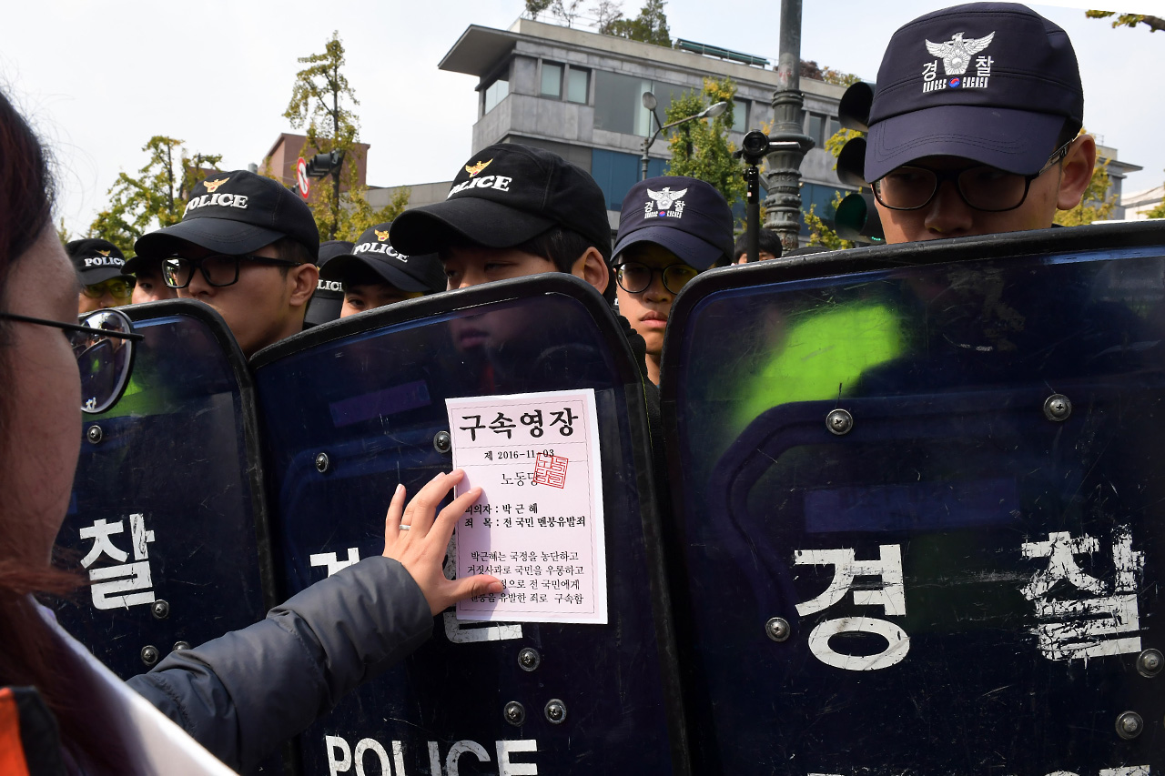 3일 오전 청와대로의 진출을 시도하던 노동당 당원들이 경찰에 가로막히자 '박근혜 구속영장' 유인물을 경찰의 방패에 붙이고 있다.