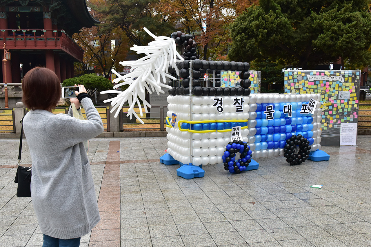 한 시민이 '물대포 공격 1년, 물대포 추방의 날 선포 대회' 행사장에 풍선으로 만들어져 있는 경찰의 물대포 조형물을 스마트폰을 이용해 사진을 찍고 있다.