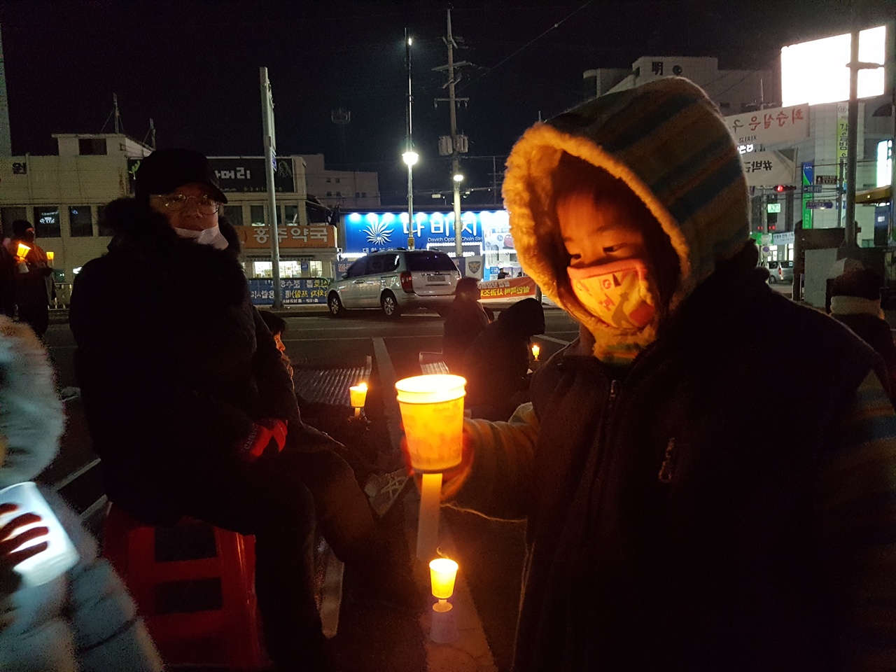  엄마의 손을 잡고 나온 아이가 촛불을 들고 있다