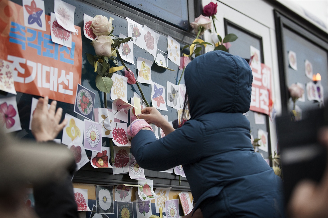 박근혜-최순실 국정농단을 규탄하는 제5차 범국민행동 집회에 참가한 한 시민의 자녀가 무등을 타고 경찰차벽에 꽃 스티커를 붙이고 있다.