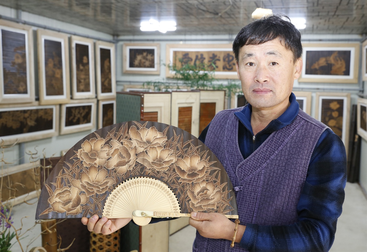 박동석 씨가 자신의 작품 전시실에서 부채에 새긴 대나무 조각작품을 들어보이며 대나무 조각의 세계에 대해 설명하고 있다.