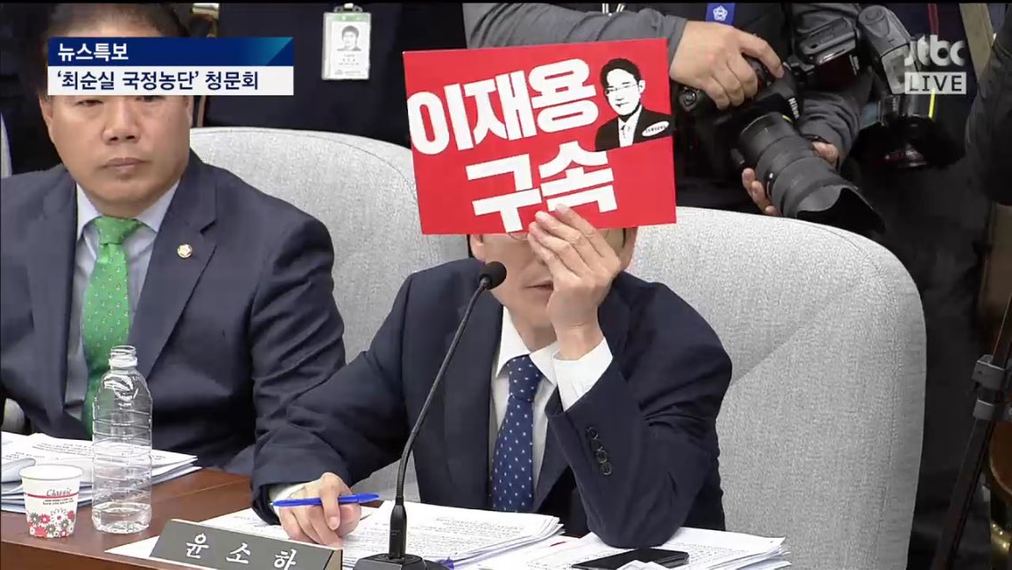 정의당 윤소하 의원이 6일 열린 '최순실 국정농단 의혹 국정조사 특위' 1차 청문회에서 이재용 삼성전자 부회장에게 '이재용 구속'이 적힌 손팻말을 보여주고 있다. 