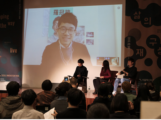 스카이프로 띄운 스크린 속에서 컨퍼런스 연사와 참석자에게 이야기를 들려주는 네이선 로의 모습. 앉아있는 사람은 왼쪽부터 스와하라 다케시, 페이 위, 김형근. 