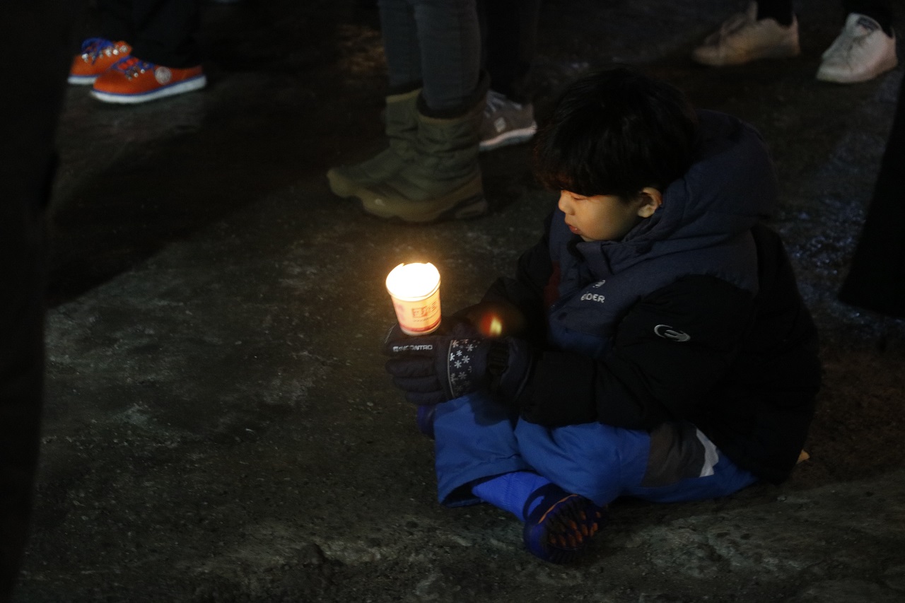 어른 시민들 사이에서 아이가 주저않아 촛불을 바라보고 있다.