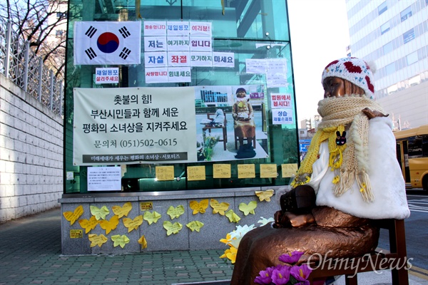  부산 일본총영사관 앞에 있는 평화의 소녀상. 옆에 있는 지하철 엘리베이터 외곽벽에 일본을 옹호하는 내용과 '일본군 위안부 한일합의 규탄'하는 내용의 글이 붙어 있고, 부산교통공사는 오는 15일까지 부착물을 철거하라고 했다.