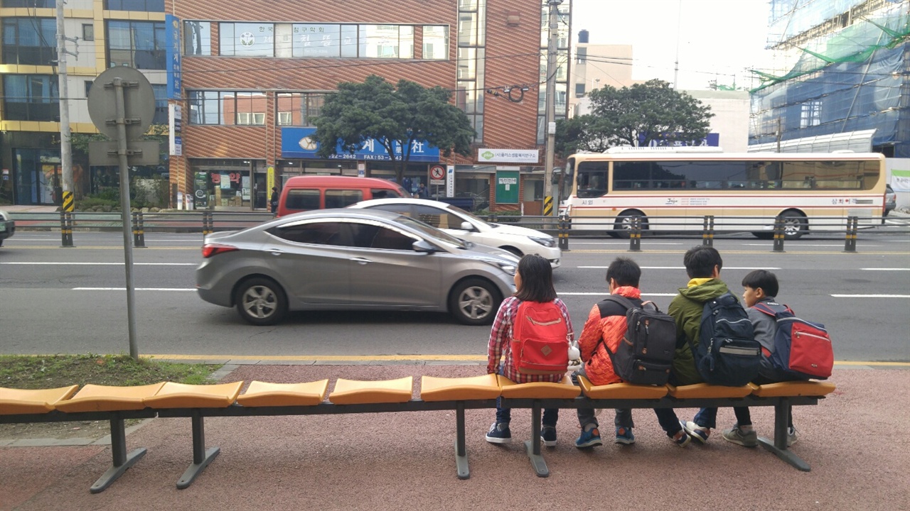 임시 버스정류장에서 서지 않는 버스를 기다리는 아이들