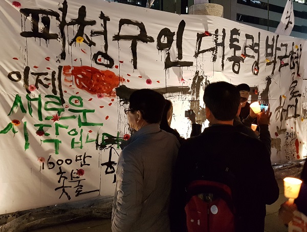 11일 저녁 헌재 박근혜 대통령 탄핵인용 이후 광화문 광장에 등장한 대형 현수막에 '이제 새로운 시작입니다'라는 글을 읽고 있는 촛불시민들이다.