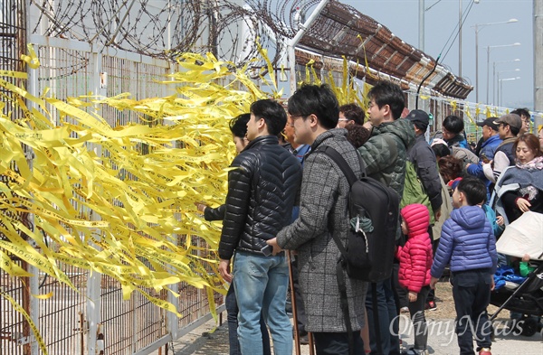  1일 오후 시민들이 목포신항에서 철제 담장 너머로 보이는 세월호를 바라보고 있다. 담장에서는 시민들이 매어 놓은 노란색 추모리본이 바람에 휘날리고 있다.  