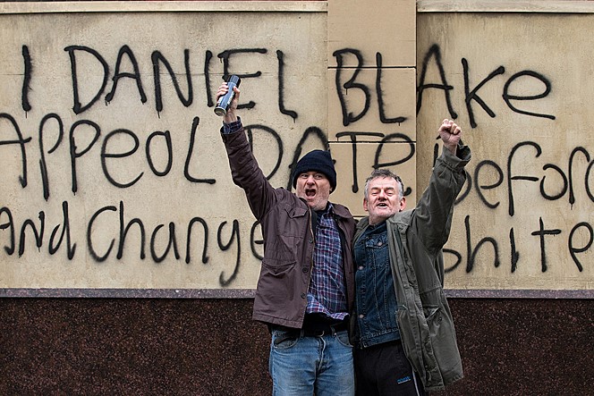  영화 <나, 다니엘 블레이크> 스틸컷. 심사기관의 벽에 자신의 이름을 페인트칠한 다니엘이 길거리의 시민과 함께 환호를 내지르고 있다.