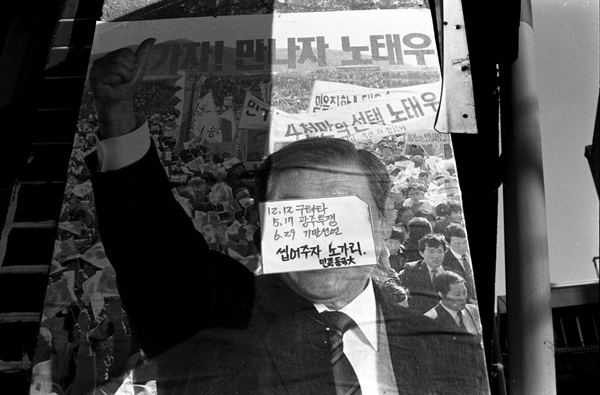 1987년 12월 12일 독재정권을 연장하기 위해 출마한 노태우 대통령 후보의 선전포스터와 그 위에 붙어 있는 동국대학교 학생들의 비난 글