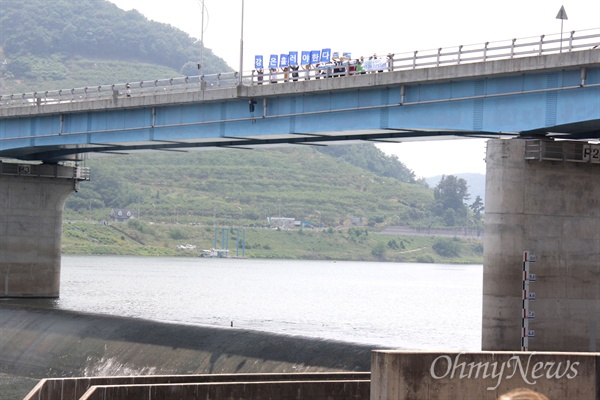 1일 오후 2시 낙동강 창녕함안보 수문이 개방되자 물이 흘러 내리는 가운데, 교각 위에서 시민들이 "강은 흘러야 한다"는 손팻말을 들고 서 있다.