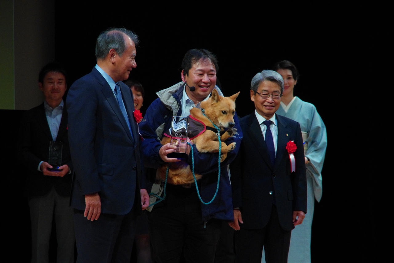 피스윈즈재팬의 오니시 켄스케 대표가 유메노스케를 안고 일본경제신문에서 부여하는 상을 받고 있다. 
